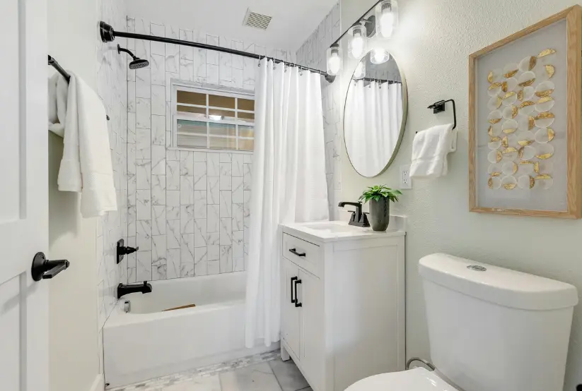 Modern small bathroom renovation featuring white marble tiles, black fixtures, a white vanity, and minimalist decor.
